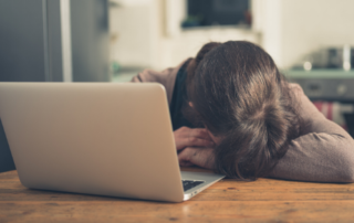 person with their head down in their arms, in front of their laptop, appearing sad or frustrated