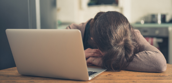 person with their head down in their arms, in front of their laptop, appearing sad or frustrated