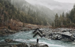 rocky river and mountain landscape with an adventurer contemplating their path forward
