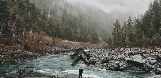 rocky river and mountain landscape with an adventurer contemplating their path forward