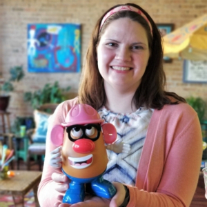 photo of Amanda Pink wearing a pink cardigan sweater, smiling and holding a Potato Head toy