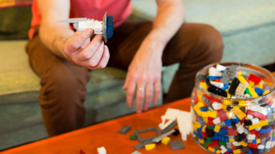 photo of a person holding up an assembly of legos at Catalyst Ranch, with a coffee table strewn with multicolored lego bricks.